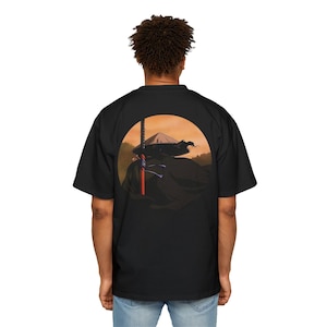 May include: Black oversized t-shirt featuring a graphic of a samurai with a sword and a mountain landscape inside a circular orange background. The samurai is wearing a black robe and hat. The sword has a red handle.