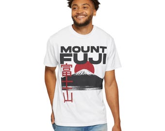 Op de afbeelding: Wit T-shirt met een afbeelding van Mount Fuji, een rode zon en een zwart berg silhouet. De tekst "MOUNT FUJI" staat boven de berg, met Japanse karakters eronder. Het T-shirt wordt door een persoon gedragen.