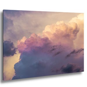May include: A vibrant photograph of a cloudscape, featuring a dramatic display of colors. The image showcases large, fluffy clouds in shades of purple, pink, and gold, set against a backdrop of a pale blue sky. The composition captures the dynamic nature of the sky.