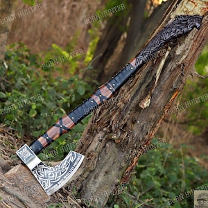 May include: A handcrafted axe with a silver blade featuring intricate Celtic knotwork and the inscription "SCORCHED WOLF MENTALITY PREVAILS." The axe has a wooden handle wrapped in black leather and accented with brown wood and brass studs. The axe head is adorned with a carved wolf head.