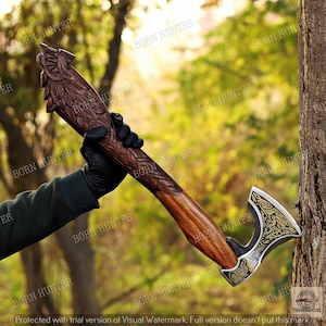 May include: A hand axe featuring a dark brown wooden handle intricately carved with feather-like patterns and a wolf head at the top. The metal axe head displays a silver and gold-colored engraved wolf design with ornate scrollwork detailing.