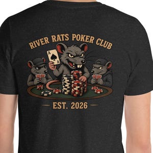 May include: A dark charcoal grey t-shirt featuring a graphic on the back of three cartoon rats playing poker at a table with chips and cards. The text reads RIVER RATS POKER CLUB and EST. 2026 in a tan font. The central rat holds an ace of spades.