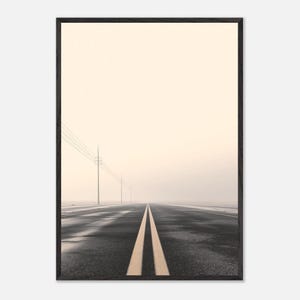 Könnte beinhalten: Gerahmter Druck mit einer langen, geraden Straße mit gelben Mittellinien, die in einen dunstigen, blassen Himmel führt. Stromleitungen verlaufen parallel zur Straße. Der Asphalt wirkt nass und reflektiert das Licht.