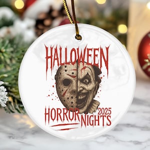 May include: A white ceramic Halloween ornament with a gold string. The ornament features a split design with a hockey mask on one side and a scary clown face on the other. The words "HALLOWEEN HORROR NIGHTS 2025" are printed in red.