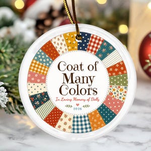 Könnte beinhalten: Ein rundes, weißes Keramikornament mit einem zentralen Textbereich, der Coat of Many Colors, In Loving Memory of Dolly und 2026 liest. Der Rand besteht aus einem bunten Patchwork-Muster mit verschiedenen Blumen-, Vichy- und Punktmustern.