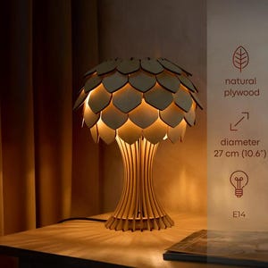 Puede incluir: Lámpara de mesa de madera con un diseño único. La lámpara presenta una pantalla con forma de pétalos y una base con listones de madera verticales. Diámetro: 27 cm. Fabricada en madera contrachapada natural, emite una luz cálida.