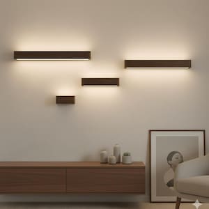 May include: A modern interior design featuring several rectangular, dark brown wall-mounted lights with a warm, inviting glow. The lights are arranged in a staggered pattern on a light-colored wall, above a wooden cabinet.