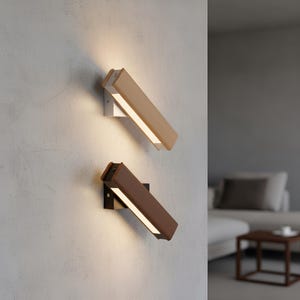 May include: Two modern wall sconces with rectangular light fixtures. One is light brown with a silver bracket, the other is dark brown with a black bracket. Both are angled and emit a warm white light.