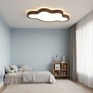 May include: A cloud-shaped ceiling light fixture with a brown wooden frame and a bright white interior. The light is mounted in a child's bedroom with a light blue wall, a bed, and a small wooden bookshelf.