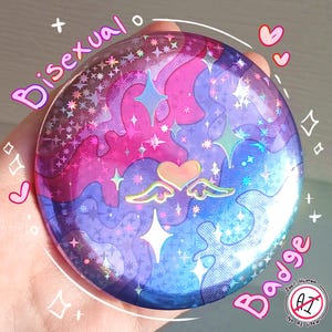 May include: A circular pin-back button featuring a holographic finish with a wavy pattern in shades of pink, purple, and blue. The design includes a central heart with small wings, surrounded by various star shapes and sparkles throughout.