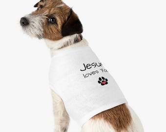 May include: A white dog vest featuring the text "Jesus loves You" in black script, with a paw print and red heart. The dog has brown, black, and white fur.