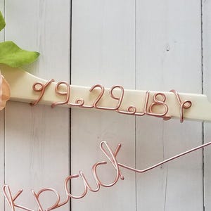 May include: A white wooden hanger with the date "9.29.18" and the word "Luck" written in rose gold wire.