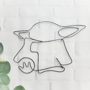 May include: A black wire sculpture of a popular fictional character, resembling a small, green alien with large ears. The sculpture is made of a single continuous piece of wire, creating a minimalist and modern design.