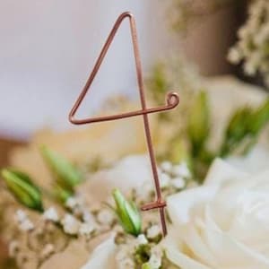 Può includere: Un numero di tavolo in filo di rame a forma di numero quattro. Il numero è in piedi in un arrangiamento floreale.