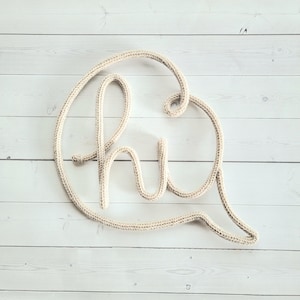 May include: A white crocheted word "hi" in a speech bubble shape against a white wood background.