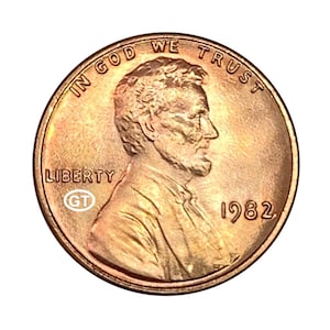 Puede incluir: Una moneda estadounidense de color cobre de 1982, con un perfil de Abraham Lincoln. La moneda tiene las inscripciones "IN GOD WE TRUST" y "LIBERTY". La moneda también tiene las iniciales "GT".