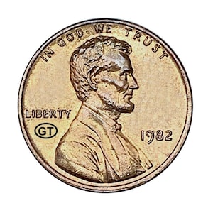 Puede incluir: Una moneda de cobre de 1982 de Lincoln. La moneda presenta un perfil de Abraham Lincoln, las palabras "IN GOD WE TRUST" y "LIBERTY". El año "1982" es visible. La moneda tiene una marca "GT".