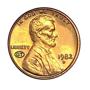 Puede incluir: Una moneda de un centavo de dólar estadounidense de color cobre con un perfil de Abraham Lincoln. La moneda tiene el texto "IN GOD WE TRUST" y "LIBERTY" junto con el año "1982". La moneda también tiene las iniciales "GT".