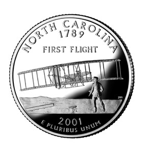 May include: A United States quarter coin depicting a biplane in flight, with a person on the ground. The coin has the text "North Carolina 1789 First Flight" and "2001 E Pluribus Unum" around the edge.