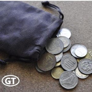 May include: A dark gray drawstring pouch with coins spilling out. The coins are various sizes and shapes, with visible markings. The pouch is on a textured surface. The image includes the letters "GT" in a white oval.