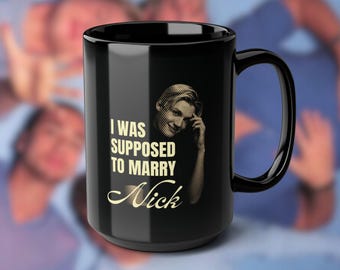 Puede incluir: Taza de cerámica negra con asa curva. La taza presenta el texto "I WAS SUPPOSED TO MARRY Nick" en una fuente dorada, junto con una imagen en tonos sepia de una persona.