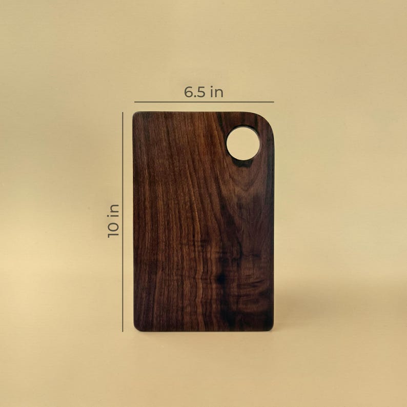 May include: A rectangular wooden cutting board with a dark brown finish. It measures 10 inches in height and 6.5 inches in width. A circular hole is cut out of the top right corner.