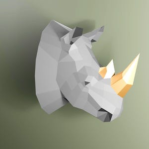Peut inclure: Une sculpture géométrique en forme de tête de rhinocéros grise avec une corne dorée. Le rhinocéros est monté sur un mur vert clair. La sculpture est faite de nombreuses formes triangulaires plates.