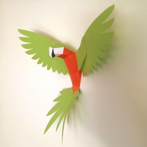 May include: A three-dimensional paper craft parrot in a flying pose with wings spread wide. The bird features bright lime green wings and tail feathers, with a vibrant orange chest and a white and black beak detail, constructed from folded paper.