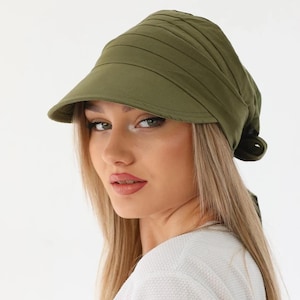 Könnte beinhalten: Olivgrüner Visor-Hut mit strukturiertem, plissiertem Design. Der Hut hat einen gebogenen Schirm und eine Bindung am Rücken. Der Hut ist aus einem weichen, matten Stoff gefertigt. Dieser Hut ist ein stilvolles Accessoire für den Sonnenschutz.