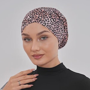 May include: A black long-sleeved top with a high neckline and a decorative ruffle. The top is paired with a leopard print head covering in shades of pink and brown. The outfit is simple and elegant.