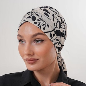 Könnte beinhalten: Ein cremefarbener Turban mit einem schwarzen Blumenmuster. Die Kopfbedeckung ist hinten gebunden. Die Person trägt ein schwarzes Hemd mit Knöpfen.