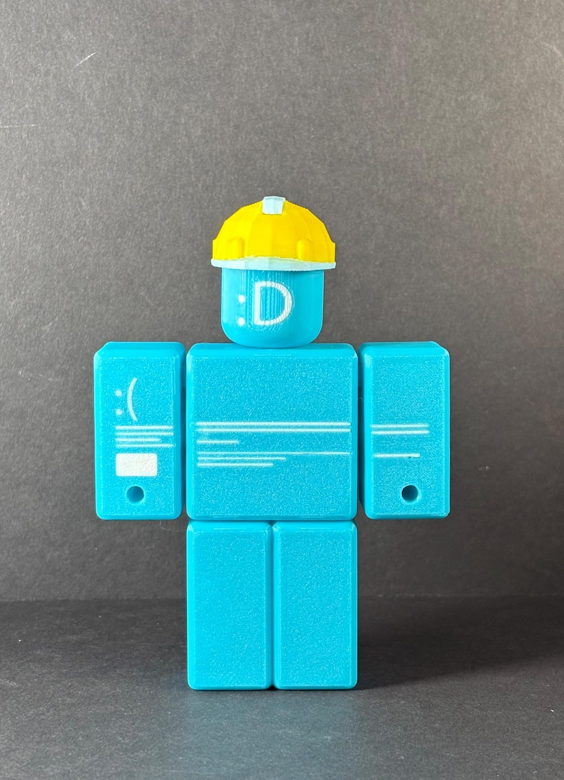 May include: A turquoise-colored block figure with a yellow hard hat. The head displays a smiling face with the letter "D". The figure has rectangular arms and legs, with a sad face on the left arm.