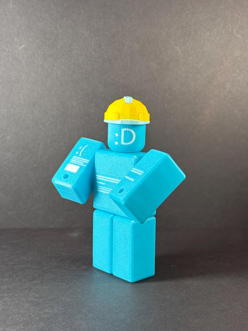 May include: A turquoise-colored, block-shaped figure with a yellow hard hat. The figure has a face with a colon and the letter "D". The figure's arms are angled outward. The figure is a 3D-printed toy.
