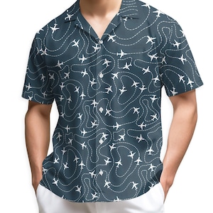 May include: Short-sleeved button-up shirt with a dark teal background and a white airplane pattern. The design features airplanes following dotted lines, creating a travel-themed aesthetic. The shirt has a classic collar and a relaxed fit.