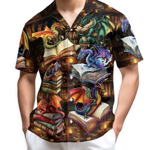 Puede incluir: Camisa de manga corta con diseño de fantasía. El estampado de la camisa muestra coloridos dragones posados sobre libros abiertos sobre un fondo de biblioteca. Los dragones son de varios colores, incluyendo rojo, verde, azul y naranja.
