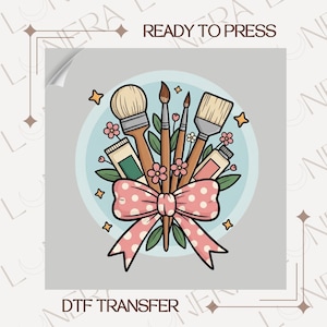 May include: DTF transfer design featuring paintbrushes, paint tubes, and a polka dot bow. The words "READY TO PRESS" and "DTF TRANSFER" are printed on the image. The design includes flowers and stars.