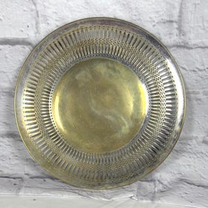 May include: A circular brass plate with a silver-toned rim. The plate has a decorative pierced border and a smooth, golden centre. This vintage plate is likely for serving or display purposes.