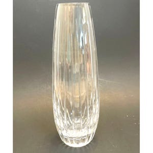 May include: A clear glass vase with vertical ribbed detailing. The vase has a tall, slender shape, widening slightly towards the top. The glass is transparent, allowing light to pass through. This decorative vase is suitable for floral arrangements.