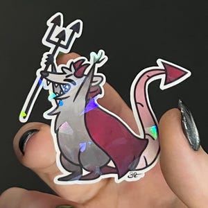 May include: A holographic sticker featuring a cartoon possum dressed as a devil, holding a trident. The possum has a red cape and a devil tail. The sticker has a shiny, iridescent finish.