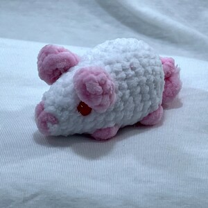May include: A handmade, plush toy mouse in white with pink accents. The mouse features pink ears, nose, and feet, with small red eyes. The soft, textured material gives the toy a cuddly appearance. This adorable mouse is a perfect gift for children.