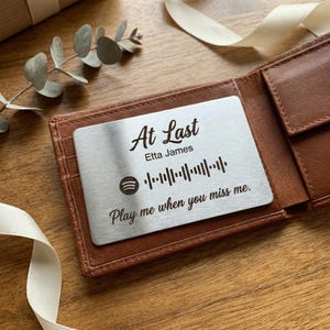May include: A white ceramic mug with a black handle and the text "But First, Coffee" in a black, bold font. The mug is sitting on a wooden surface. The mug is approximately 4 inches tall.