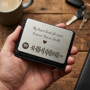 Op de afbeelding: Een zilveren metalen portemonnee kaart met de tekst "My heart beats for you. Forever Yours, Emily" en een Spotify code. De kaart zit in een zwarte leren portemonnee.