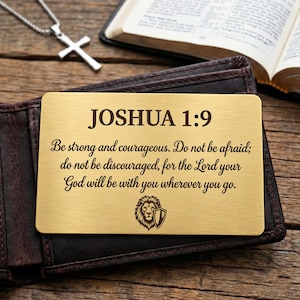 May include: A rectangular gold-toned metal wallet card featuring the engraved text JOSHUA 1:9, Be strong and courageous. Do not be afraid; do not be discouraged, for the Lord your God will be with you wherever you go, and a lion head icon.