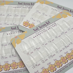 May include: Clear plastic nail sizing kits in short square and medium almond shapes are displayed. Each kit has multiple nail sizes, with measurements in millimeters. The kits are labeled with the text "Nail Sizing Kit".