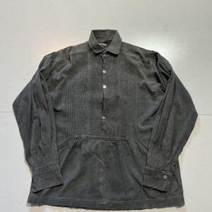 May include: A gray long-sleeve shirt with a collared neckline and button-down front. The shirt features detailed embroidery down the front and on the cuffs. The fabric has a soft, slightly worn appearance.