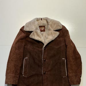 May include: A brown suede jacket with a cream-colored shearling collar and lining. The jacket has a button-up front, two chest pockets, and two side pockets. The jacket is a vintage style.