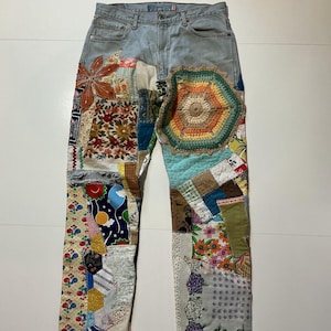 May include: Light wash denim jeans with colorful patchwork details. The patches include floral, geometric, and crochet designs in various colors. The jeans have a classic five-pocket design and a button and zipper closure.