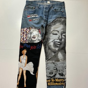 May include: Blue denim jeans with multiple Marilyn Monroe graphics. The jeans feature patches with images of Marilyn Monroe, the text "Marilyn Monroe", and the movie titles "The Seven Year Itch" and "How to Marry a Millionaire".