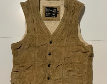 May include: A tan suede vest with a button-up front and two front pockets. The vest has a cream-colored lining and a label near the neckline. The vest appears to be vintage.