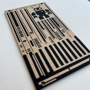 May include: A rectangular, tan-colored card with a black barcode design and a robot graphic. The robot is in the center of the card, above the barcode. The top of the card has binary code printed on it.